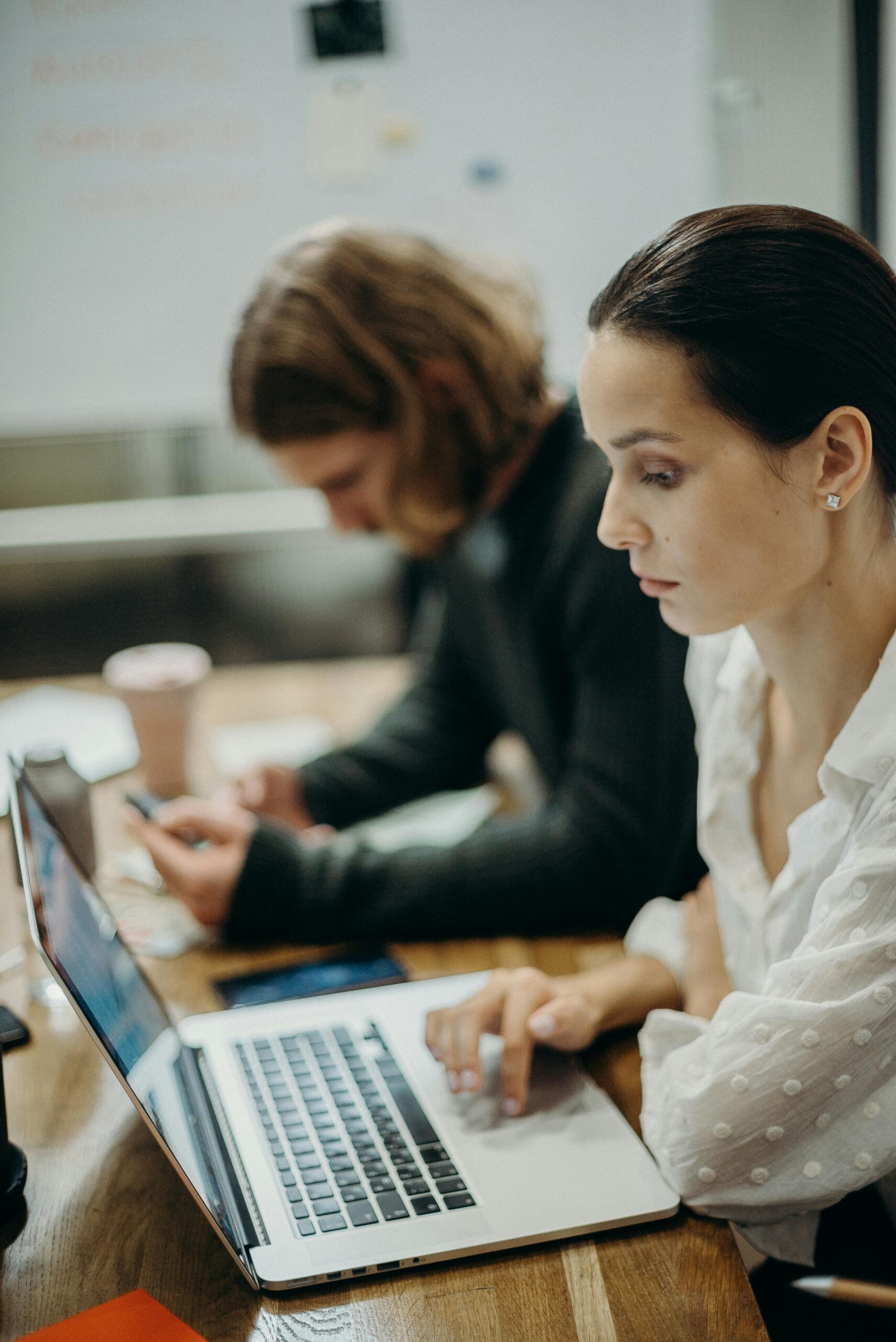 Two professionals working together at a laptop in a modern office setting.